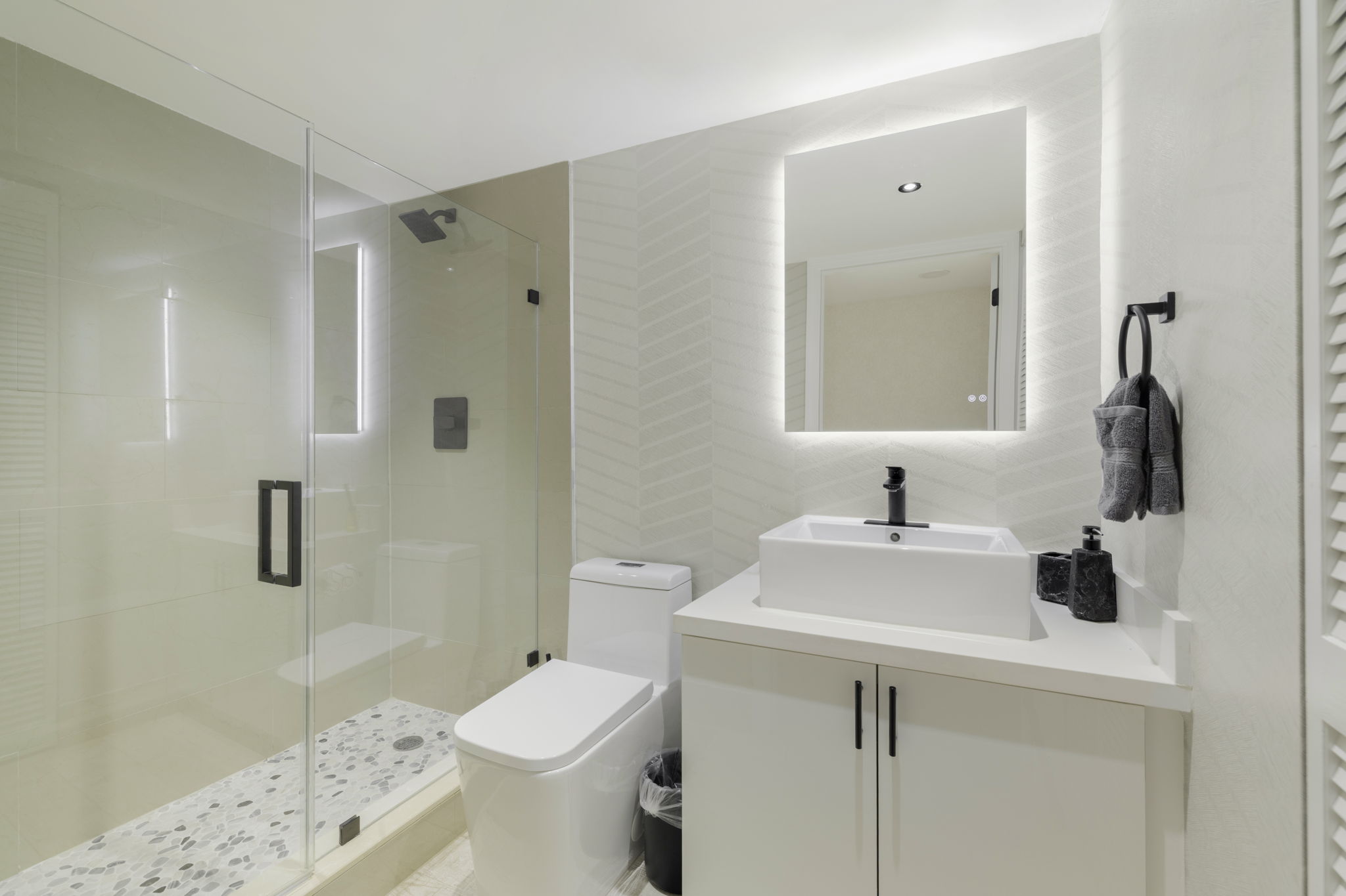 Second full bathroom with walk-in glass shower and backlit mirror